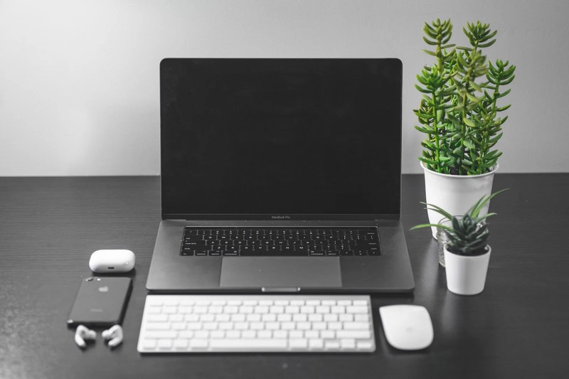 An Apple MacBook Air laptop sitting on a desk next to a charging case for AirPods Pro.