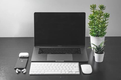 An Apple MacBook Air laptop sitting on a desk next to a charging case for AirPods Pro.